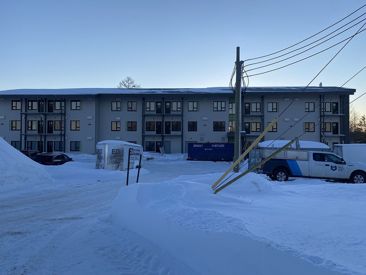Un immeuble d'appartements enneigé, avec un poteau électrique devant. Un camion arborant un logo est stationné à droite.