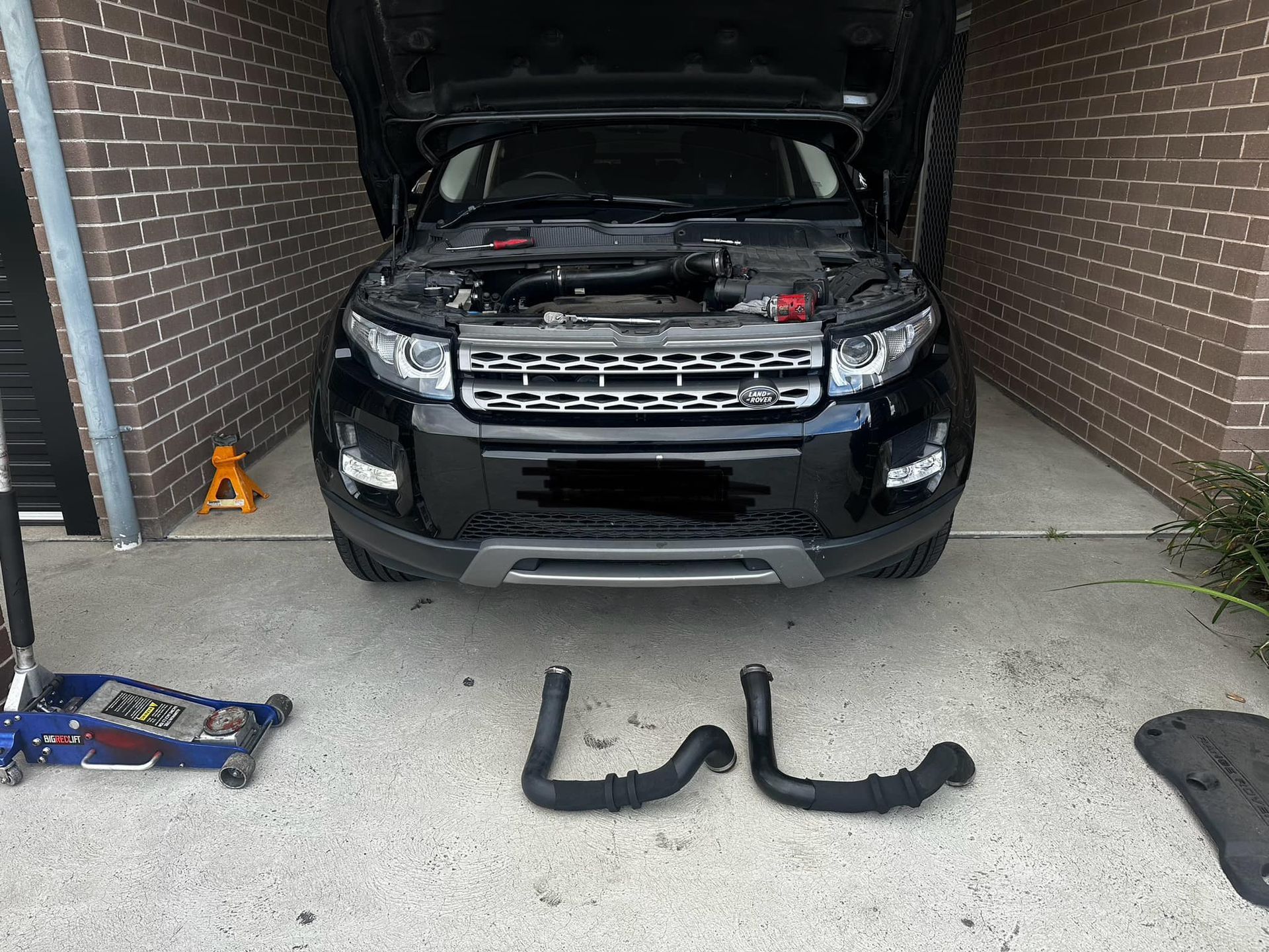 Black SUV with open hood, two hoses, and a jack; parked in a garage. — JDM Mobile Mechanical in Bankstown, NSW