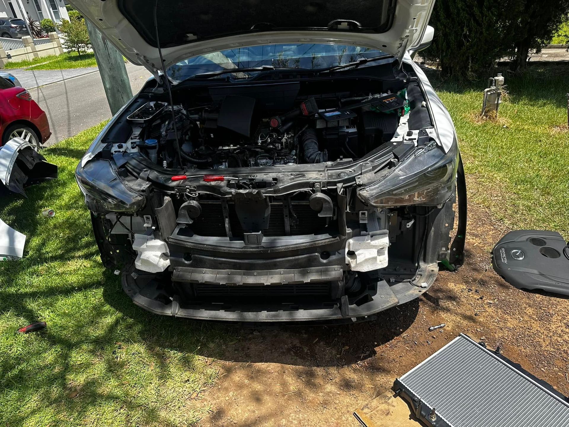 Car with open hood, front end damage. Radiator and parts scattered on grass outdoors. — JDM Mobile Mechanical in Moorebank, NSW