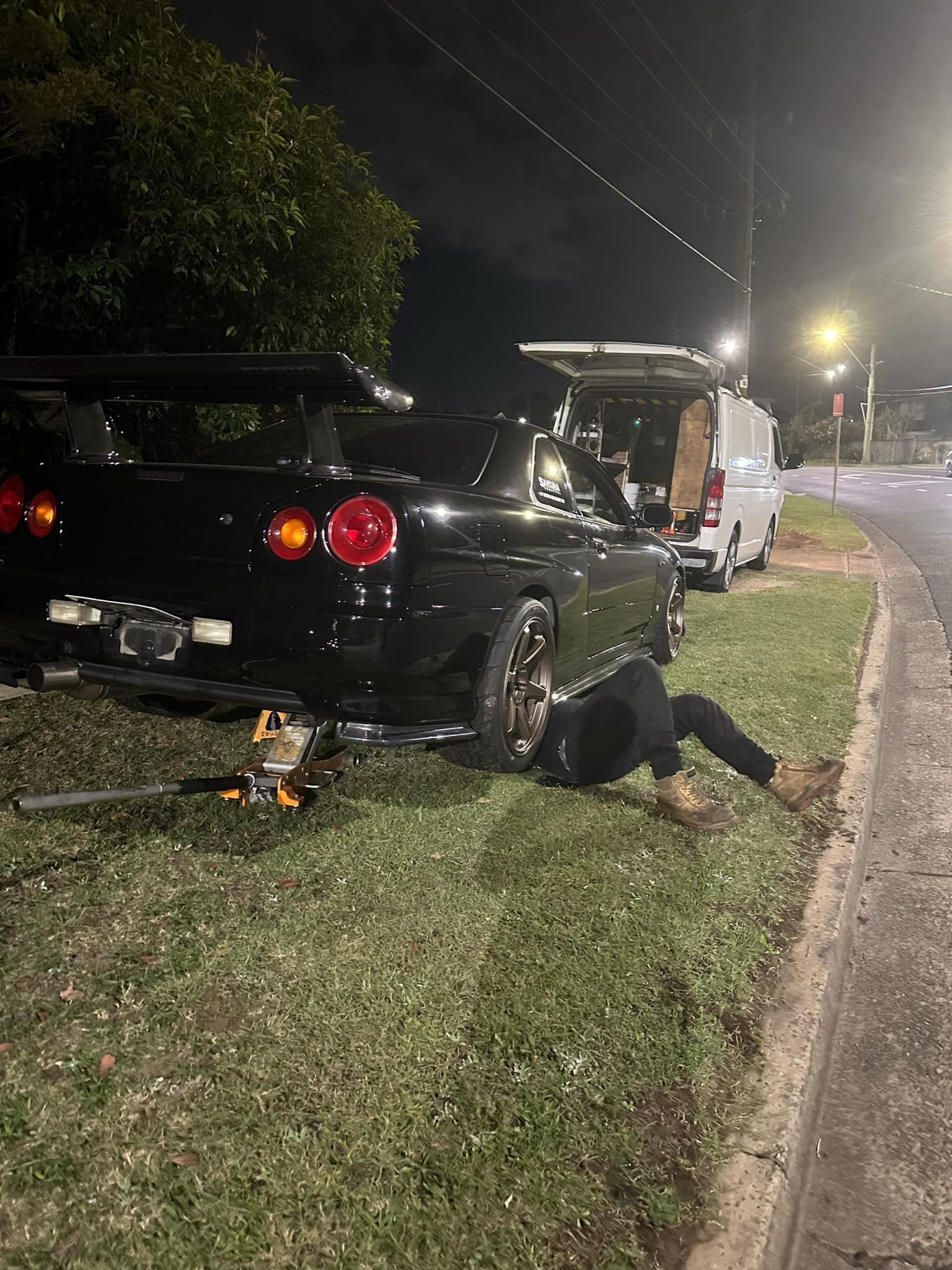 Person Working on a Black Car Parked on Grass at Night — JDM Mobile Mechanical in Holsworthy, NSW