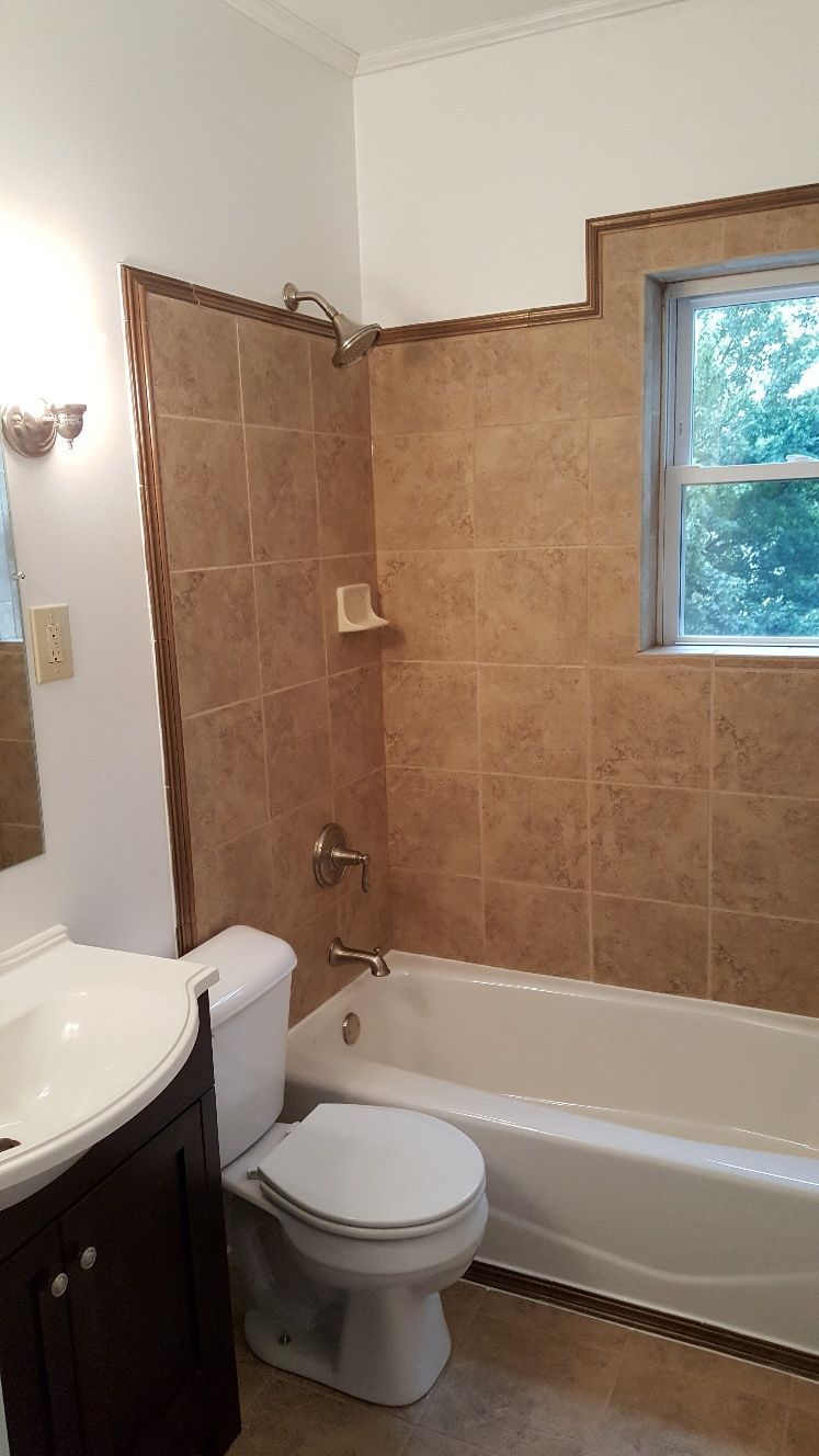 Bathroom with brown tiled shower and tub, toilet, vanity, and window.