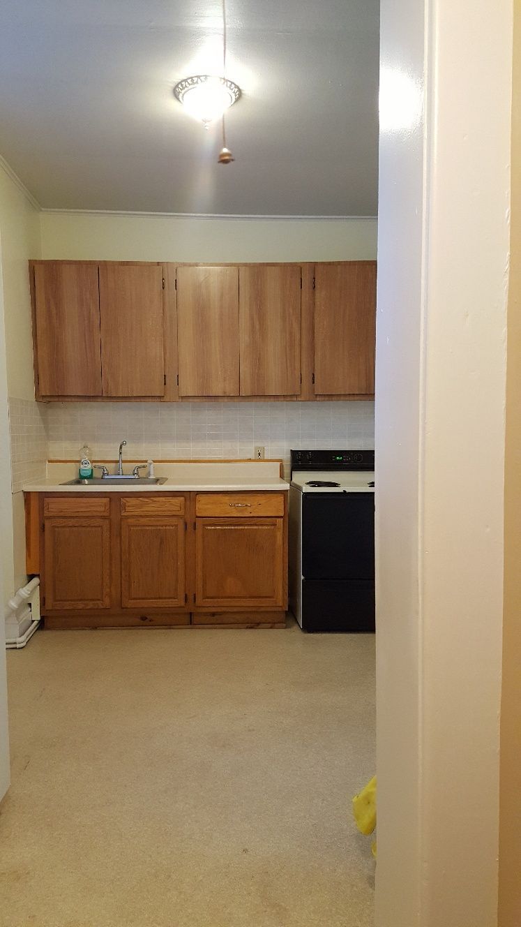 Kitchen with wooden cabinets, a sink, and a black stove. Cream-colored walls and beige flooring.