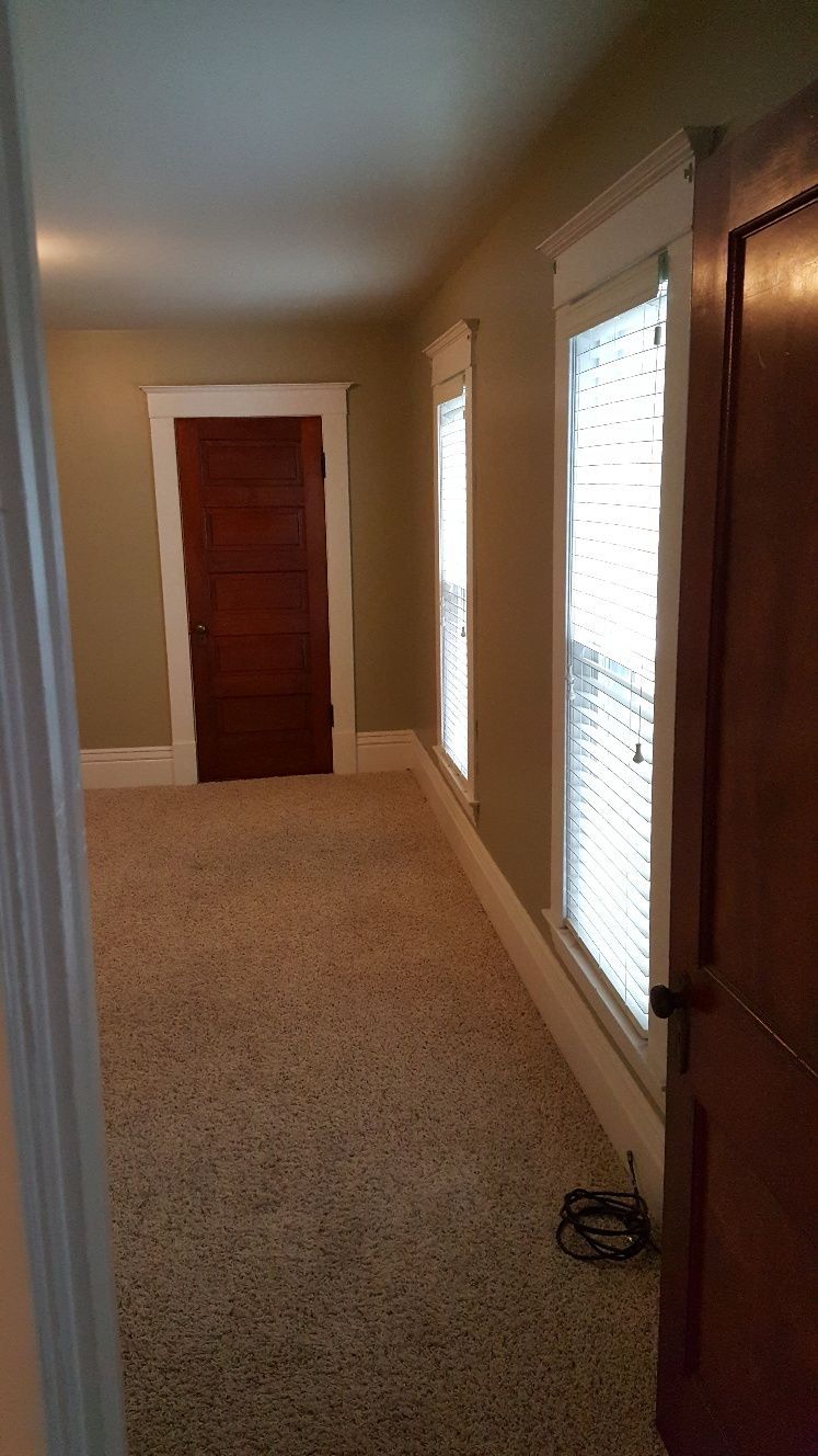 Empty room with carpet, windows, and a closed wooden door.
