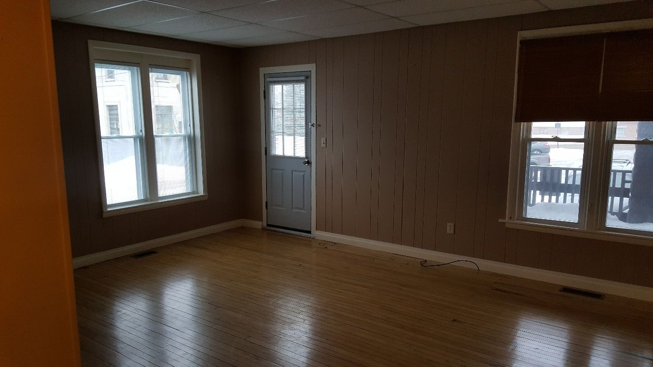 Interior room with two windows, a door, and wooden floor. Brown walls, window blinds, and natural light.