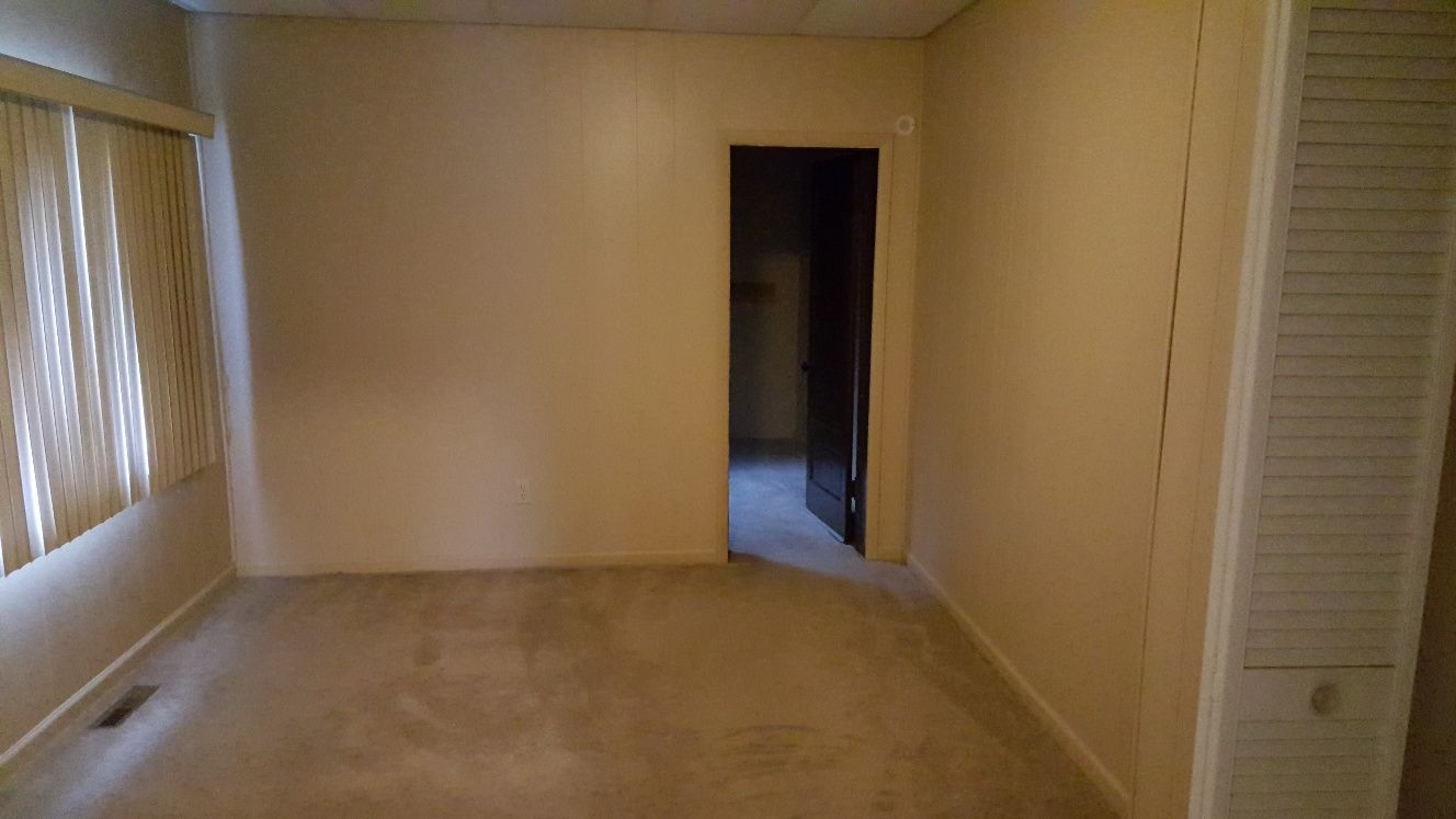 Empty room with beige walls, carpet, window with blinds, doorway, and radiator cover.