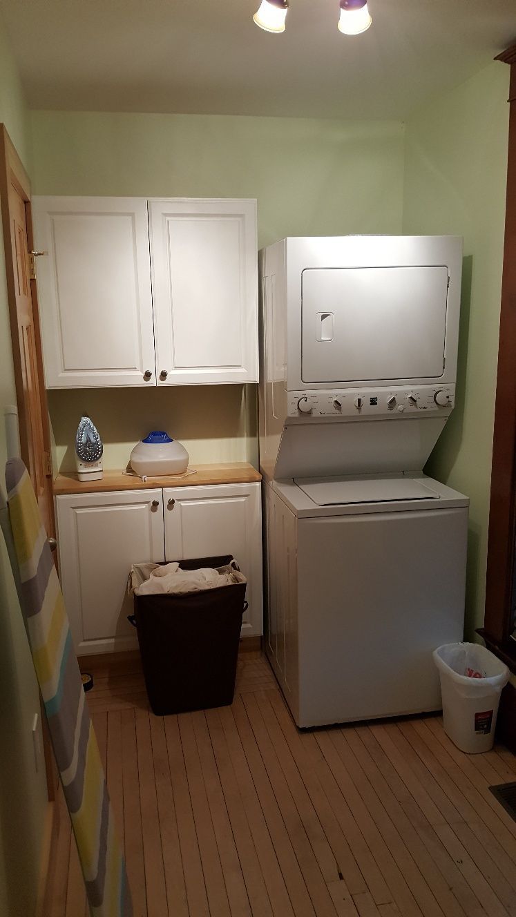 Laundry room with white appliances, cabinets, and wooden floor. Ironing board on the left.