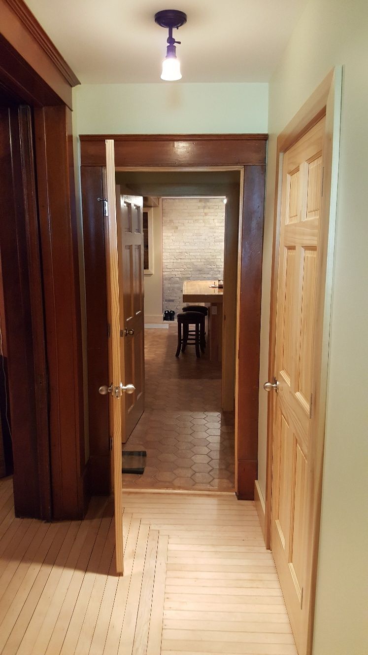 Hallway with wooden floors and doors, leading to a room with a brick wall and a table.