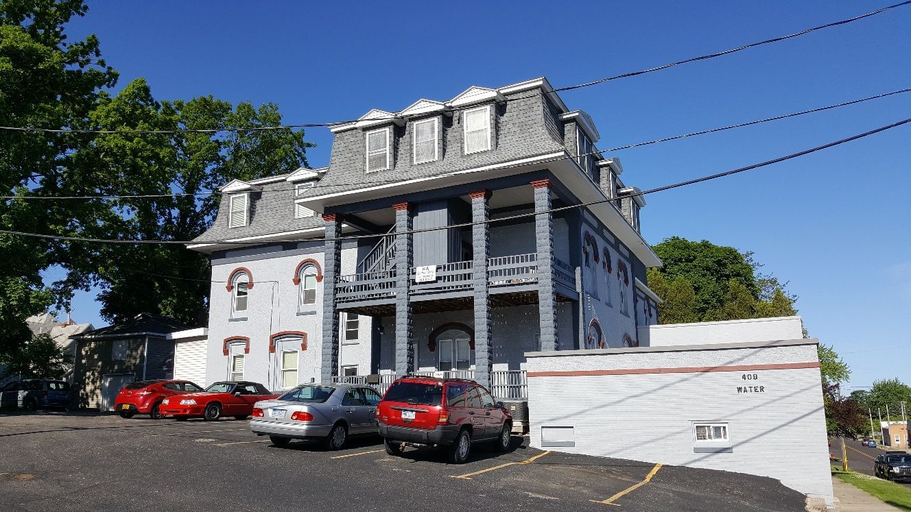 Gray multi-story building with cars parked in front on a sunny day.