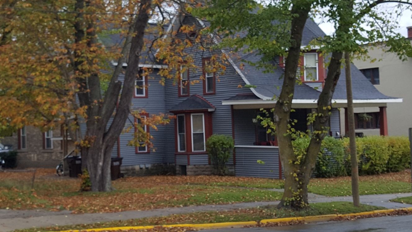 Two-story gray house with red trim, surrounded by trees with autumn leaves.