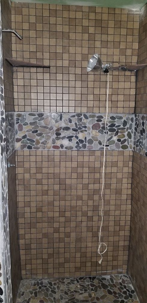 Shower stall with brown square tiles and a band of pebble tiles.