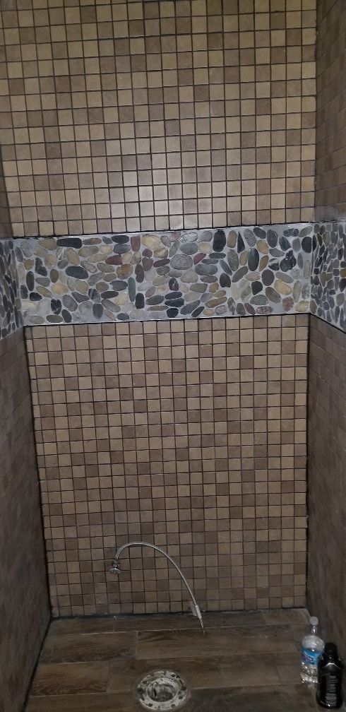 Shower stall with cube tile walls, pebble accent, and a water spout.