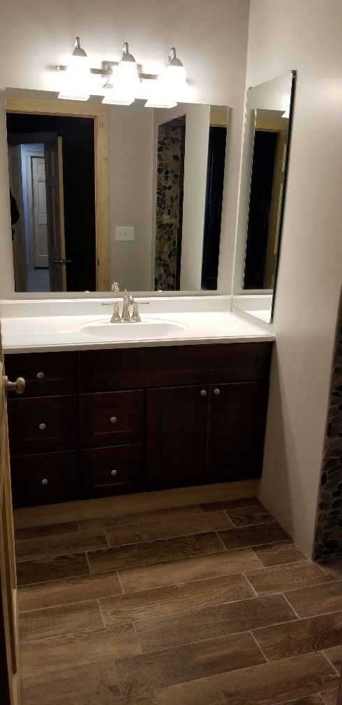 Bathroom with dark cabinets, white countertop, and wood-look tile. Large mirror and vanity lighting.