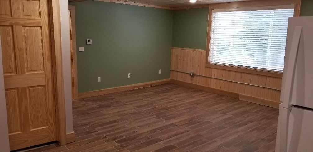 Interior of a room with green walls, wood trim, and wood-look flooring. A door and a window with blinds are visible.