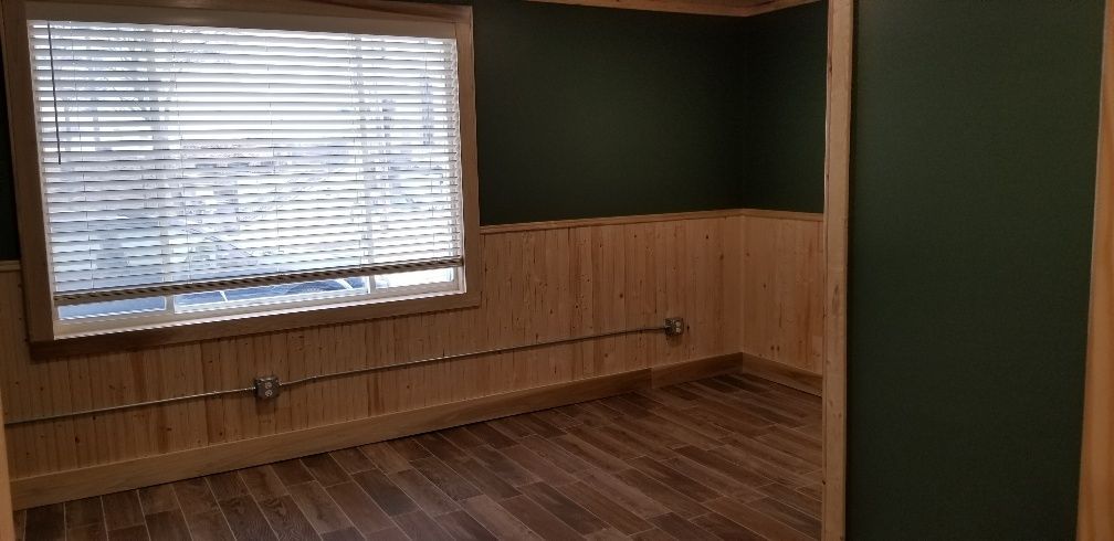 Empty room with wood paneling, dark green walls, and a window with blinds.