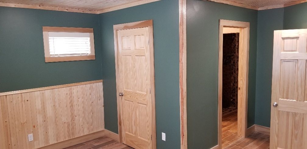 Interior room with green walls, wood trim, and doors. A small window and wood paneling are visible.