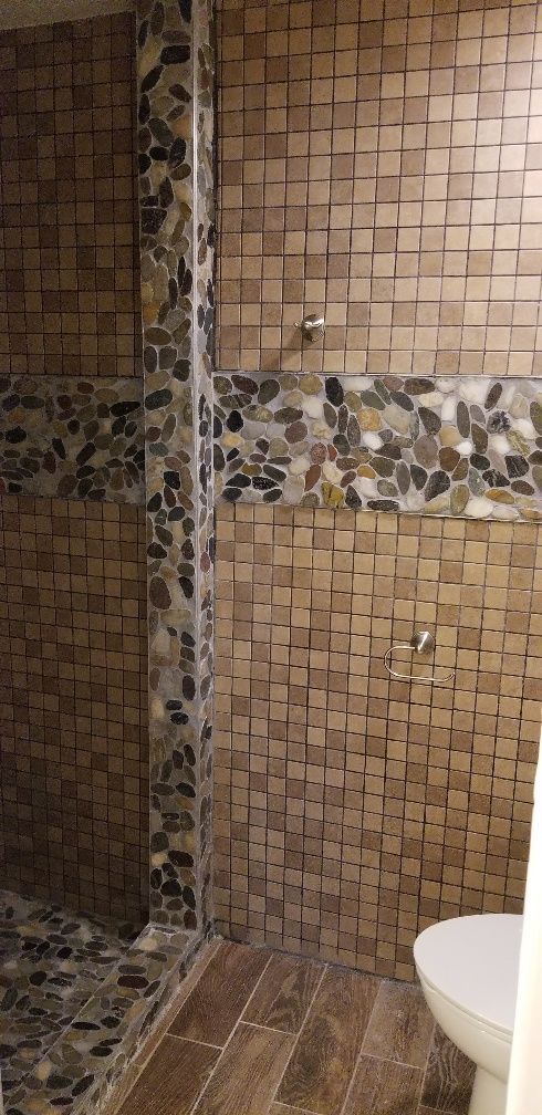 Shower with brown square tiles and dark pebble accent, with a white toilet.