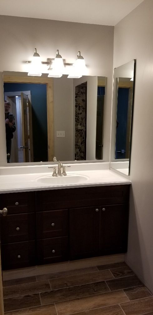 Bathroom with dark wood vanity, white countertop, large mirror, and three-light fixture.