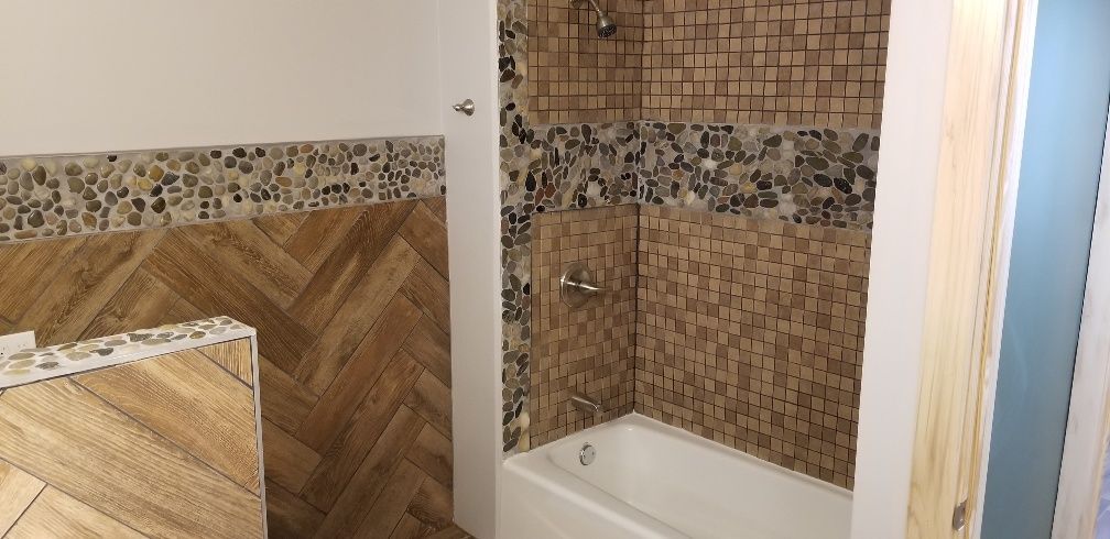 Bathroom with wooden-look tiling and mosaic accents. White tub and fixtures.