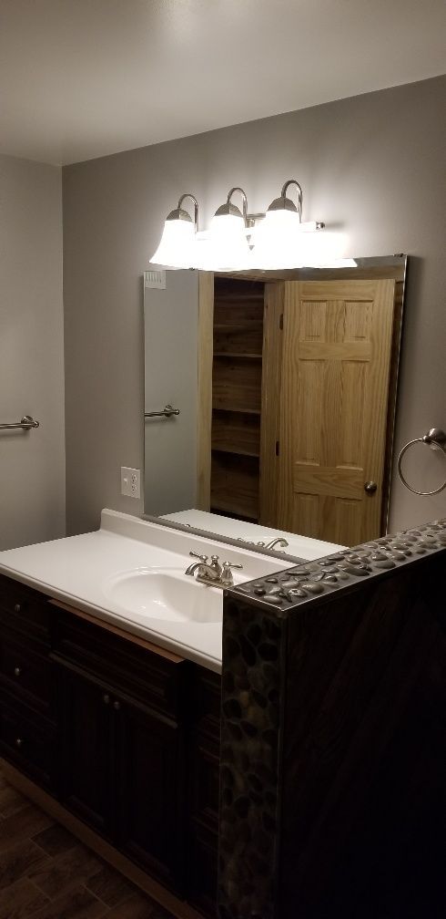 Bathroom vanity with dark wood cabinet, white countertop, and large mirror. 3-light fixture above the mirror.