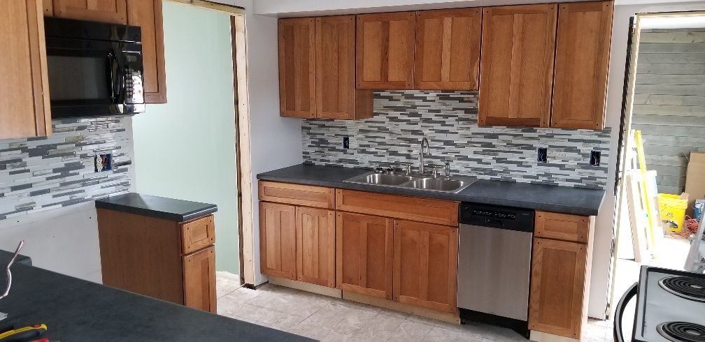 Kitchen with brown cabinets, dark countertops, and a gray and white tile backsplash.