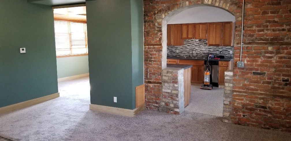 Interior view of a room with green walls and a brick archway leading to a kitchen with wooden cabinets.