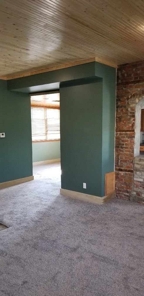 Interior of a room with green walls, a wooden ceiling, and gray carpet. There is an exposed brick wall.