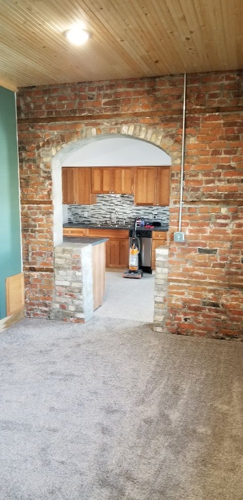 Brick archway leading into a kitchen with wooden cabinets and a stone backsplash.