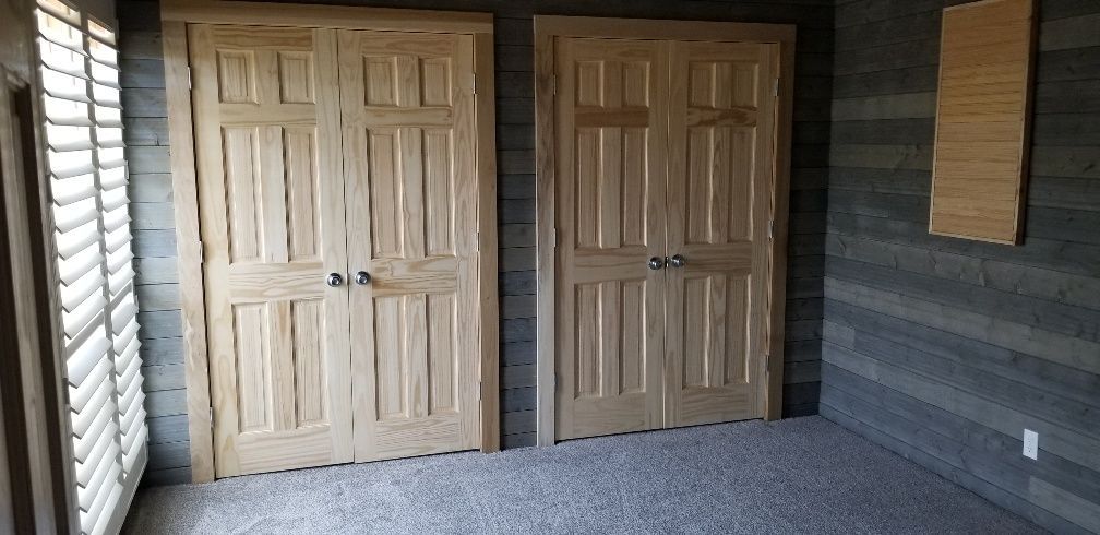 Two light wood paneled doors standing on gray carpet in front of a blue-gray paneled wall.