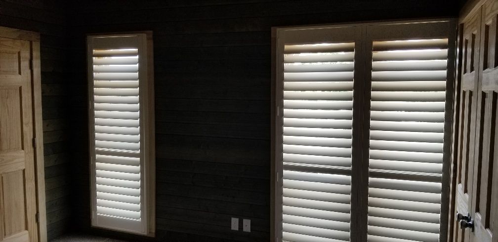 Interior view of a room with two windows covered by shutters and dark wood paneled walls.