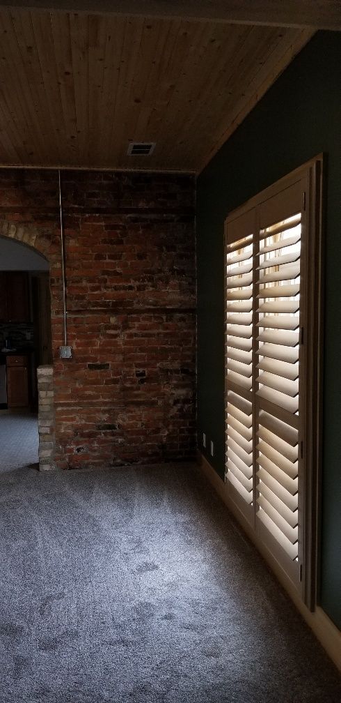 Room with brick wall, green wall with shuttered window, and gray carpet.