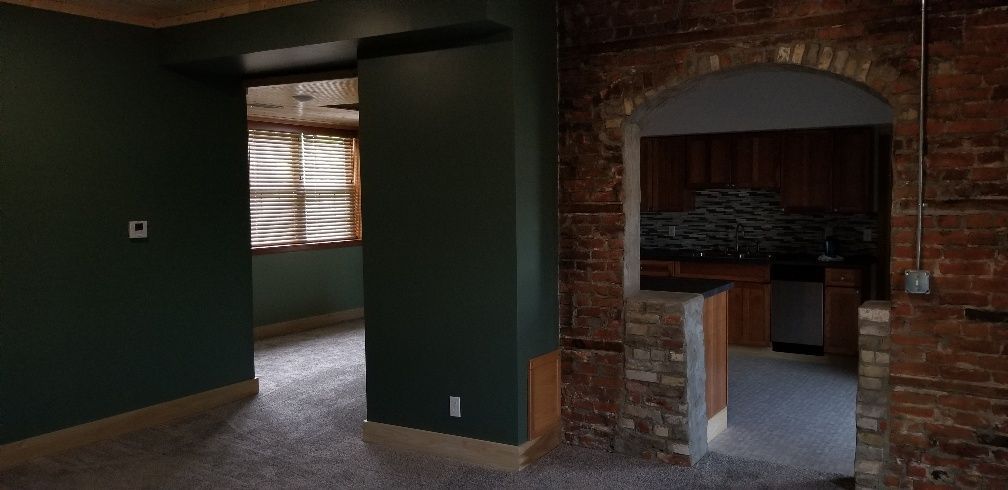 Interior with dark green walls, brick archway leading to a kitchen with wooden cabinets and dark backsplash.