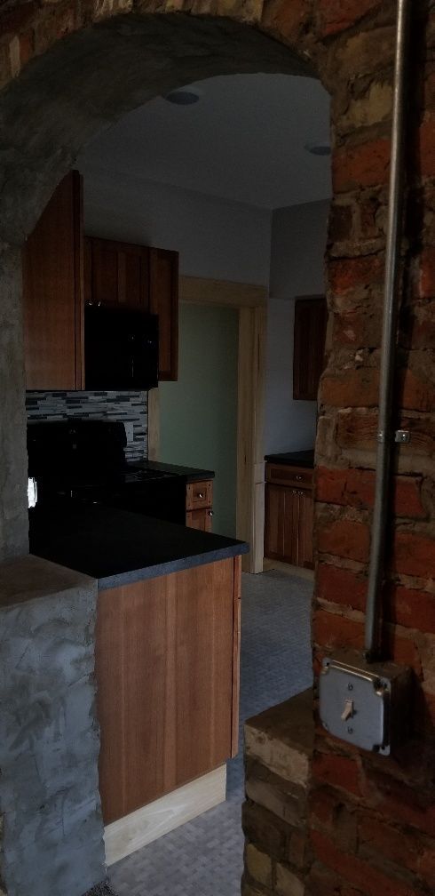 Kitchen interior with archway; brick and wood cabinets, black appliances. Electrical box on a brick pillar.