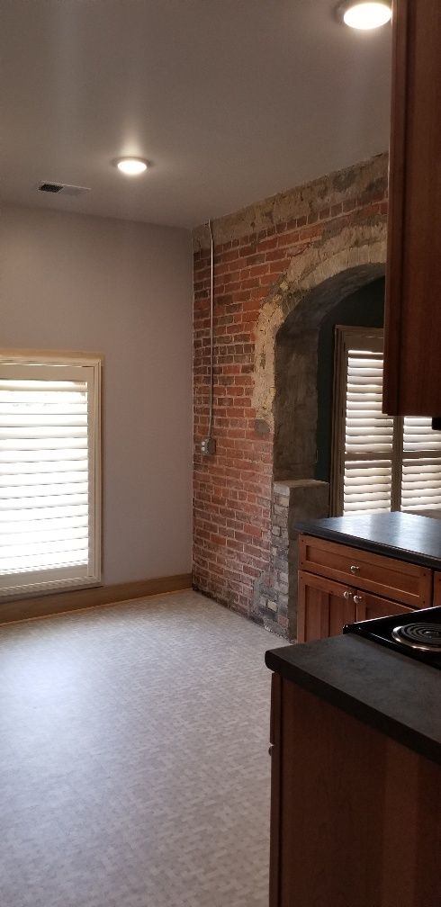 Kitchen with exposed brick wall, window with blinds, and wooden cabinets.