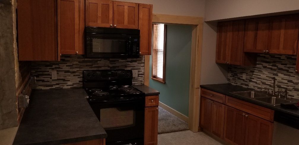 Kitchen with wooden cabinets, black appliances, and teal-colored walls.