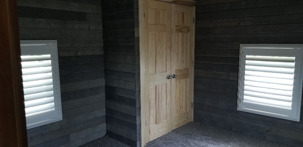Interior view of a room with wooden paneling walls, two windows, and a double-door closet.