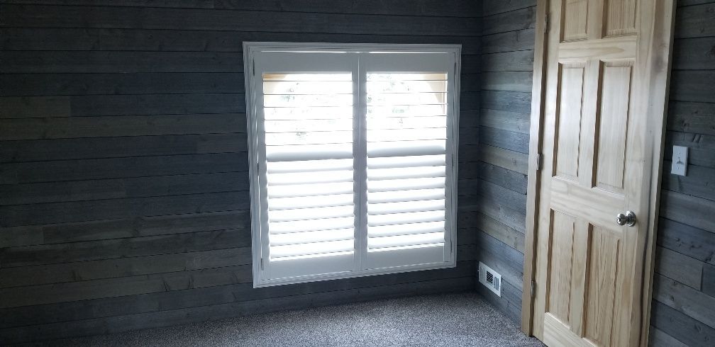 Room interior with window shutters, wooden door, and wood-paneled walls.