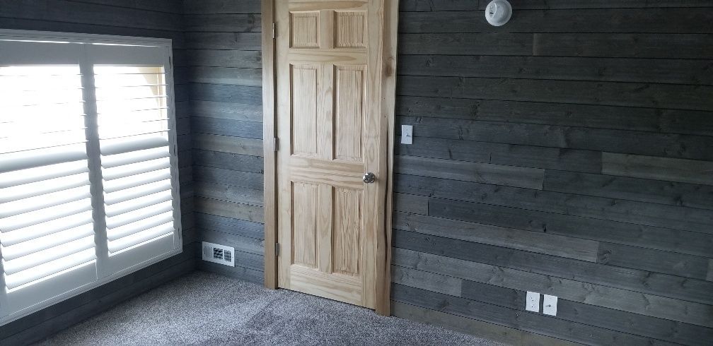 Room with wooden door, shuttered window, gray plank wall, and gray carpet.