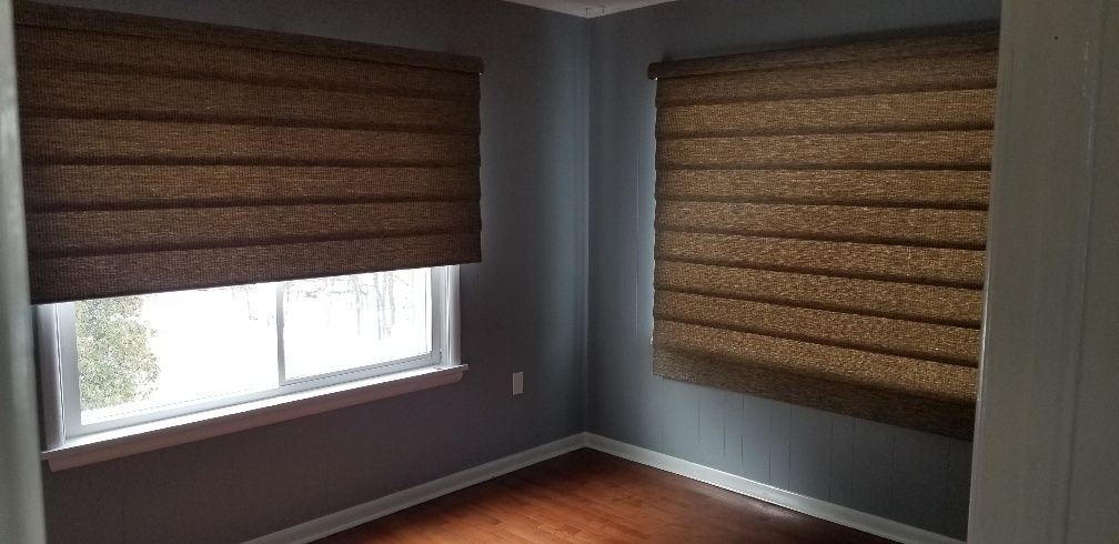 Room corner with two windows, brown shades, gray walls, and hardwood floors.