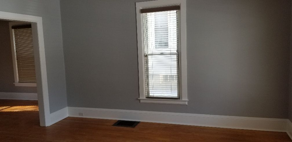 Empty room with wooden floor, gray walls, a window with blinds, and a doorway.