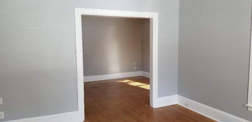 Interior of a room with gray walls, white trim, and a doorway leading to another room.