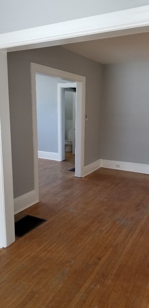 Empty room with gray walls, white trim, and hardwood floors. Open doorways lead to other rooms.