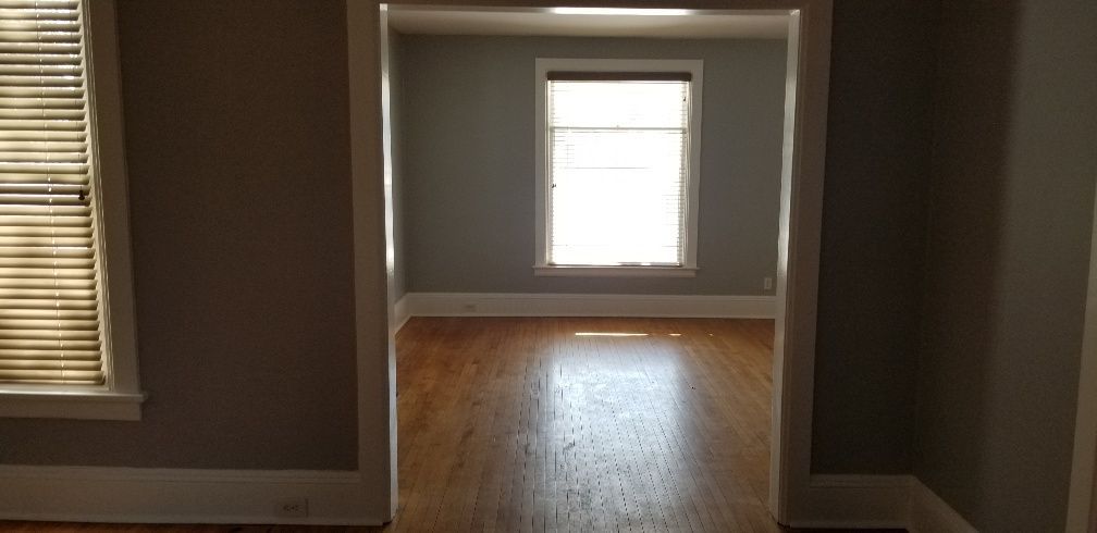 Interior view of a doorway, leading to a room with a window. The room has hardwood floors.