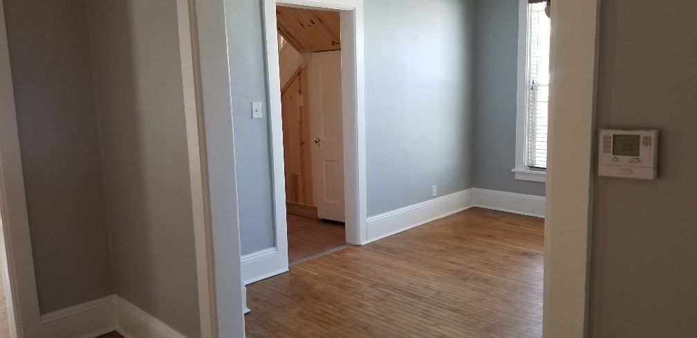 Interior view of a house showing a hallway and room with wooden floors and gray walls.