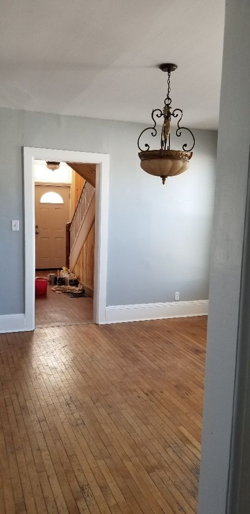 Interior view of a room with hardwood floors, gray walls, and a hanging light fixture. Doorway leads to a staircase.