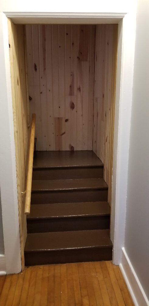 Dark wooden staircase leading upward into a recessed space, framed by white molding.
