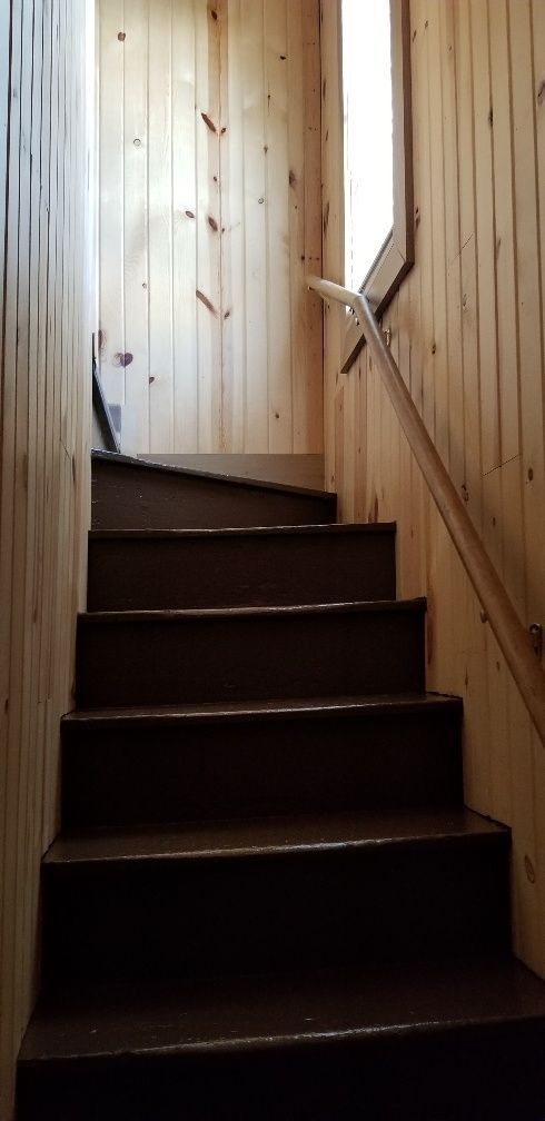 Wooden stairs leading up, surrounded by wood paneling. A window on the right provides natural light.