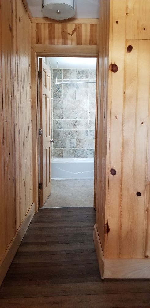 Hallway with wood paneling leading to a bathroom with a tile wall.