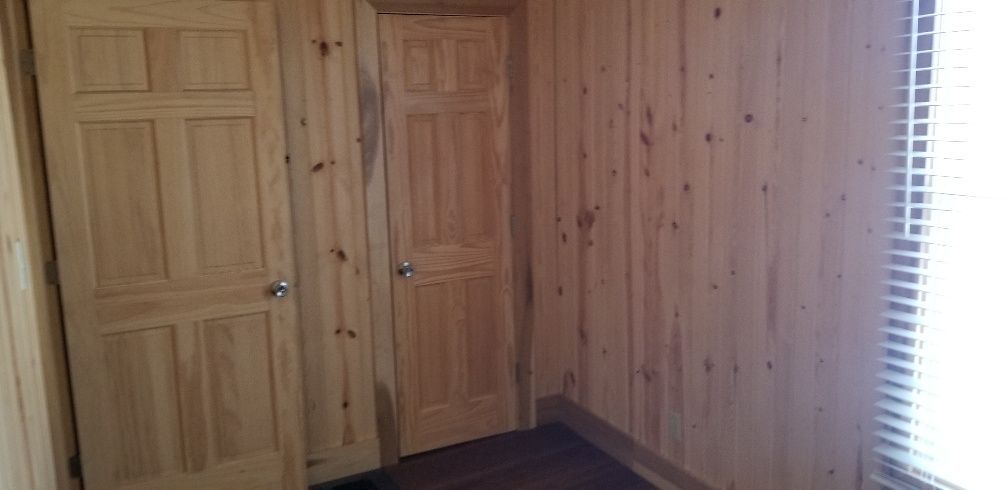 Interior view of a room with wood panel walls and doors. Blinds are visible on the right.