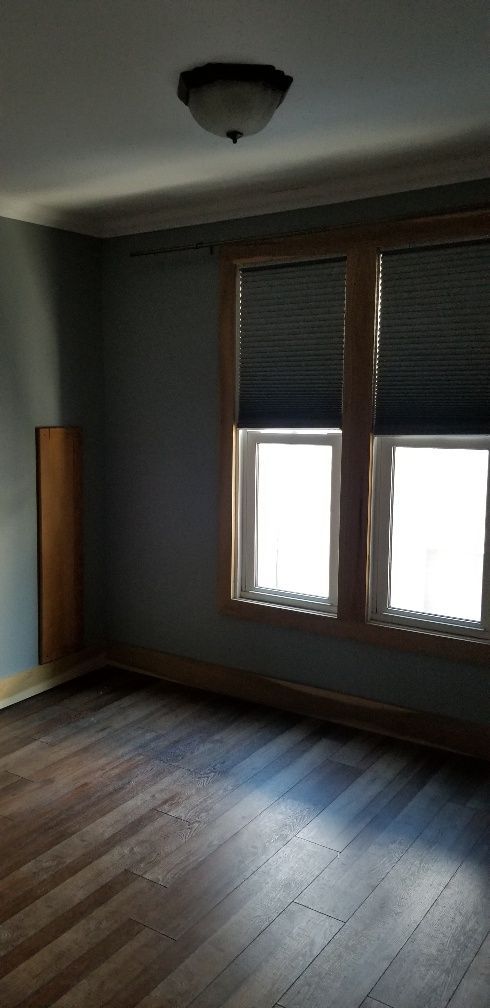 Empty room with two windows covered by blinds and hardwood floor. Blue walls and wooden trim.