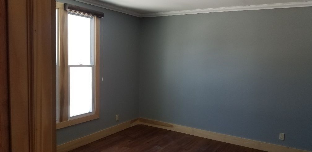 Empty room with blue walls, wooden trim and floor, and a window with a shade.